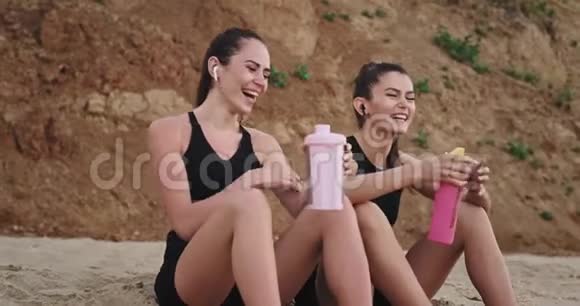 微笑着穿着运动服的大美女在海边前喝着塑料干渴的水视频的预览图