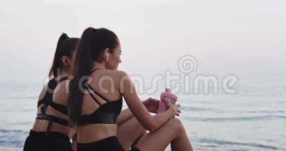 穿着黑色运动服的漂亮女士早上在海边锻炼后休息一下视频的预览图