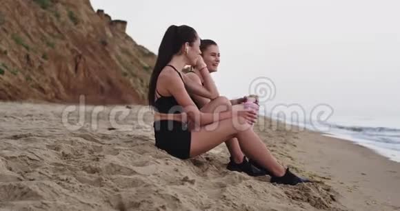 非常漂亮的两位女士在海滩上锻炼后一起享受着黑色运动服饮用水的时光视频的预览图