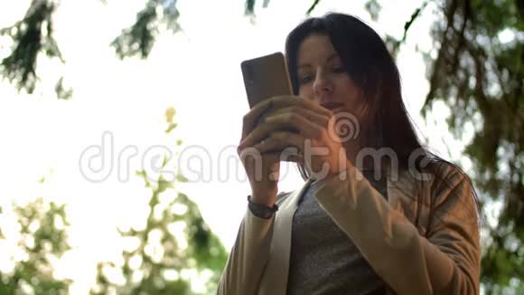 在森林户外的社交网络中年轻的黑发女人在公共聊天中输入信息视频的预览图