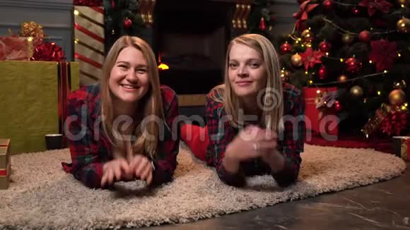 两个穿着红色格子衬衫的金发美女躺在靠近新年树或圣诞树的地毯上看上去方向不同视频的预览图