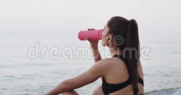 经过一次艰苦的锻炼美丽的女士喝着水在早上打坐视频的预览图