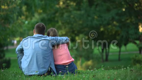 在公园的草地上拥抱和坐在草地上的年轻夫妇的后景视频的预览图