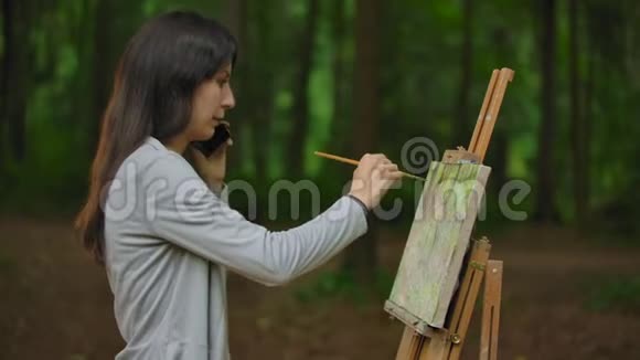 女孩艺术家在公园里画一幅风景画并通过电话交谈视频的预览图