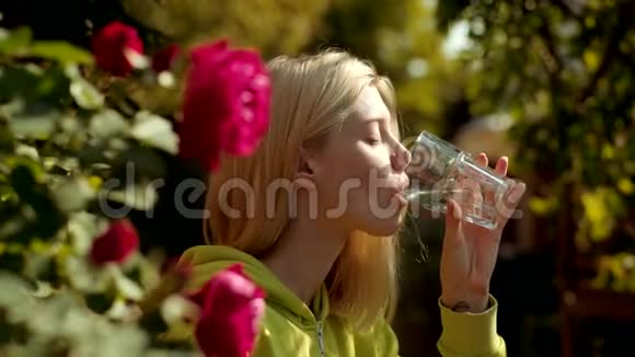 美女从绿色公园的玻璃上喝水把金发女孩的画像贴起来视频的预览图