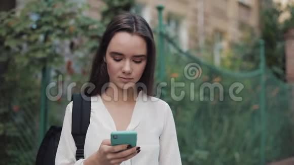 年轻美丽的学生布鲁内特女孩她的肩膀上有一个袋子使用她的现代智能手机滚动屏幕视频的预览图