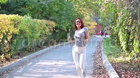 一个戴眼镜的红发美女走在街上跳舞穿灰色T恤和条纹的快乐女孩视频的预览图
