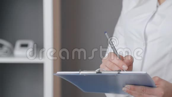 一名身穿白色外套手拿蓝色文件夹的护士的特写并在医务处记录信息视频的预览图