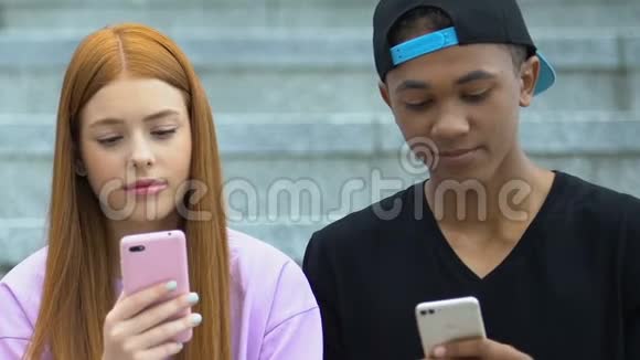 混血男少女和高加索红发女孩在户外滚动智能手机视频的预览图