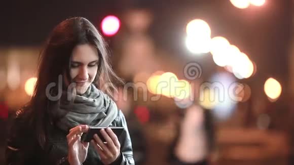 漂亮的年轻女人晚上用智能手机在寒冷的天气里街上的女士现代技术视频的预览图
