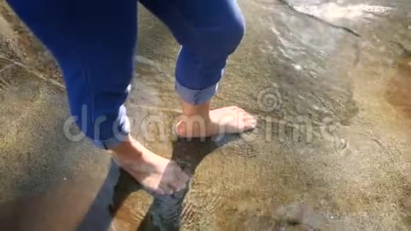 赤着脚的年轻女子在水流缓慢的溪流中溅起水花踢着腿女士们享受假期视频的预览图