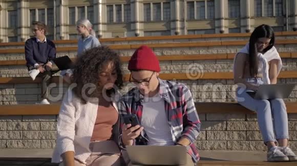 一对漂亮的夫妇在大学附近的长凳上用电话学生下课后视频的预览图