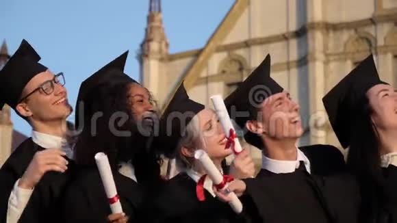 混合种族毕业的朋友穿着黑色传统长袍和帽子制作自拍智能手机视频的预览图