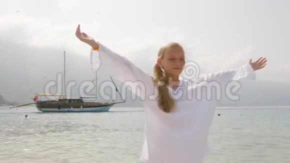 美丽的少女穿着白色长袍举起双手在海上和船舶景观旅行女孩享受海边视频的预览图