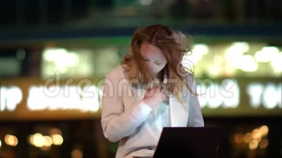 迷人的女孩自由职业者晚上坐在户外长凳上在笔记本电脑上工作风的天气视频的预览图
