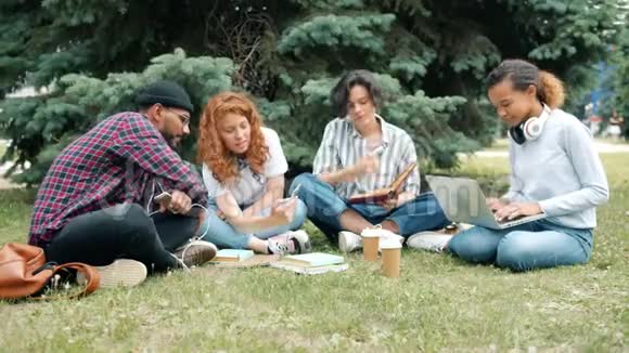 快乐的学生在户外学习带着书和笔记本电脑在草地上聊天视频的预览图