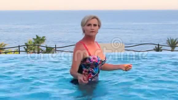 美丽的女人在无边无际的游泳池里跳舞在海滩上在腰部深的水中跳舞视频的预览图