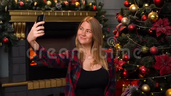 年轻漂亮的女孩或穿着红色格子衬衫的女人在背景上用圣诞树自拍视频的预览图