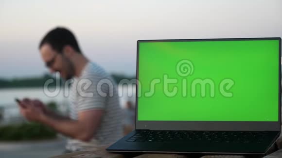 年轻的时髦男人用手机笑带有空白屏幕的笔记本电脑视频的预览图
