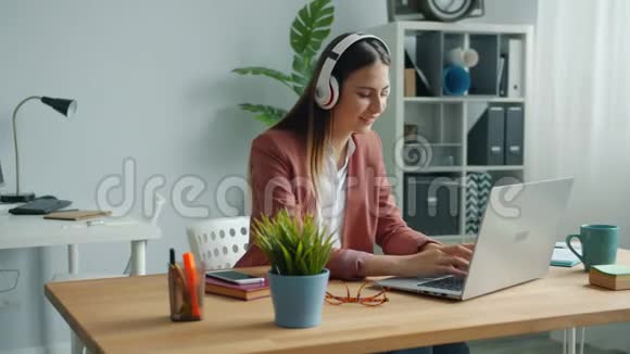 戴耳机的漂亮女士在办公室听音乐在工作中欣赏最喜欢的歌曲视频的预览图