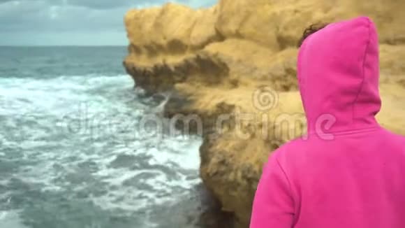 一个年轻的女人站在海中的悬崖前岩石中的大海一个女人站在背后视频的预览图