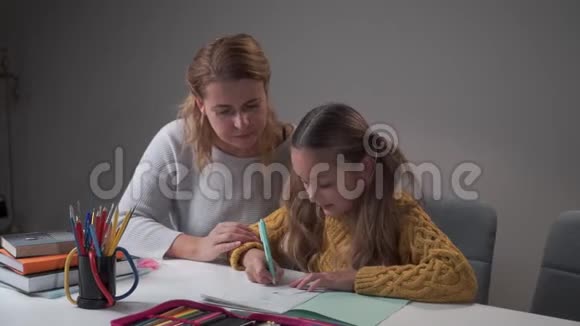 年轻的白种人女导师向可爱的小女孩解释错误作业本中的学童书写视频的预览图