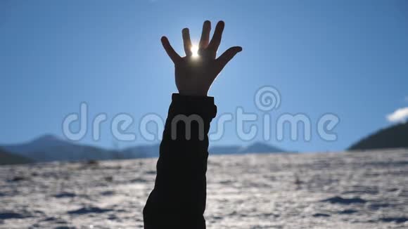 年轻人躺在雪地上手臂伸向太阳明亮的阳光透过伸出的手指视频的预览图