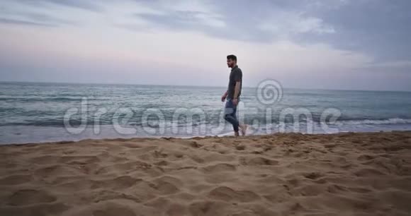 一个长着胡须的英俊男子走在海滩上那里有海浪他看上去神秘莫测视频的预览图