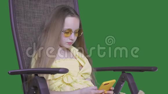 时尚少女坐在椅子上使用黄色智能手机视频的预览图
