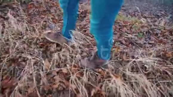 一个穿着蓝色裤子和靴子的旅行者正在草地上沿着一条森林道路行走视频的预览图