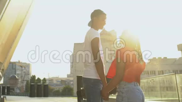 一对穿着休闲服装的黑人青年夫妇牵着手在夕阳下漫步街头视频的预览图