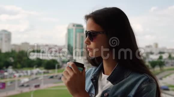 戴黑墨镜的青少年喝咖啡看城市视频的预览图