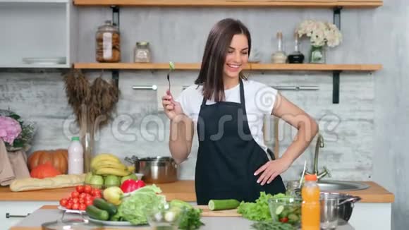 穿着围裙的年轻家庭主妇微笑着在舒适的厨房里跳黄瓜舞烹饪健康的食物视频的预览图