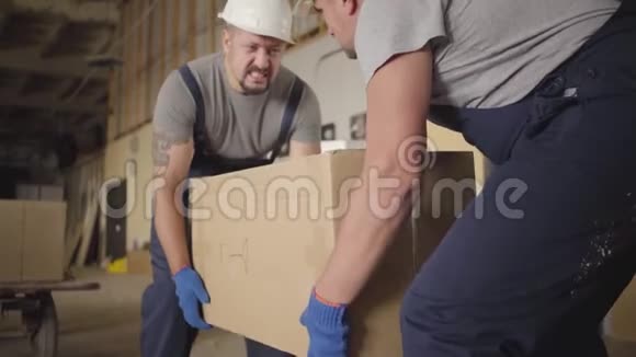 两个强壮的白人工人拿起沉重的纸板箱并在施工现场携带它成年男性视频的预览图