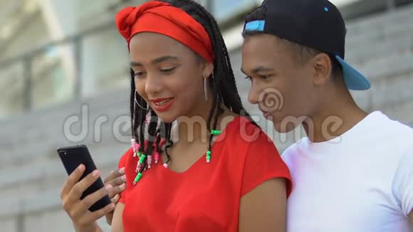拥有智能手机的黑人青少年夫妇看着最后的派对照片玩得很开心视频的预览图