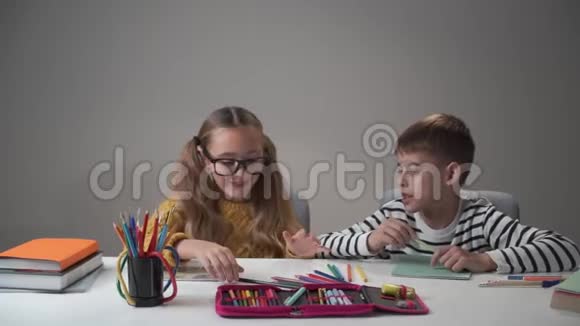 白人男孩和女孩坐在桌子旁用五颜六色的钢笔打架开朗的孩子在家玩兄弟视频的预览图