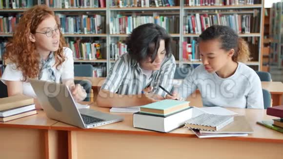 一群青少年在学校图书馆学习手提电脑和书在说话视频的预览图