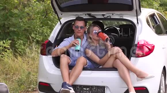 可爱的夫妇喝热茶从热水瓶坐在汽车后备箱视频的预览图