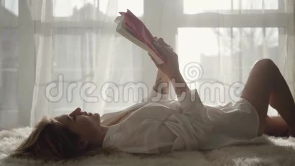 年轻的白种人女孩合上书放在胸前性感迷人的女人穿着白色衬衫躺在床上视频的预览图