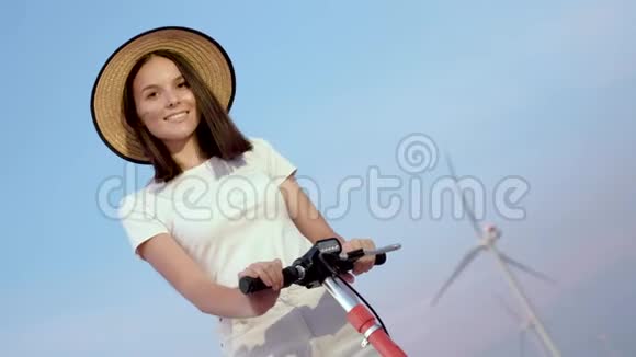 一个女孩戴着一顶优雅的草帽在风电场的背景辆电动滑板车的肖像视频的预览图