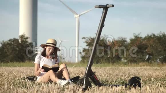 草原上一个戴着优雅帽子的女孩正在看书一辆电动滑板车站在附近背景是一辆视频的预览图