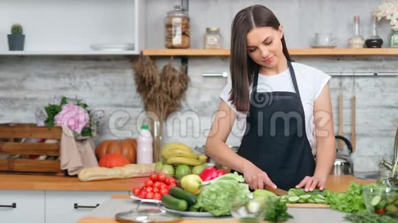 微笑着美丽的年轻家庭主妇在砧板上切鲜黄瓜在厨房里做沙拉视频的预览图