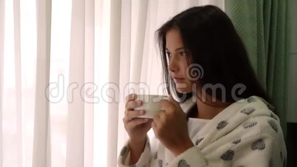 漂亮的深色头发的年轻女人穿着白色浴袍喝茶视频的预览图