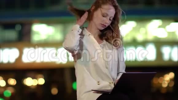 一个女商人坐在商务大楼前用笔记本电脑打字视频的预览图