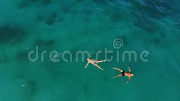 空中俯视在蓝绿色的海水中两个人游泳以星星的形式躺在背上夏季视频的预览图