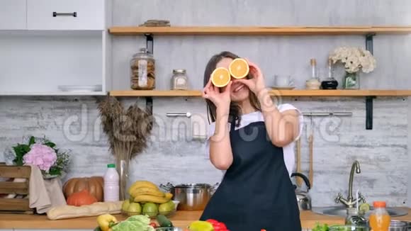 可爱的好玩的纯素的家庭主妇摆着鲜橙片在眼睛上玩得开心放大镜头视频的预览图