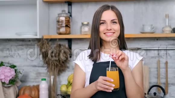 肖像美丽的微笑女孩摆姿势拿着一杯新鲜的维生素橙汁中特写视频的预览图