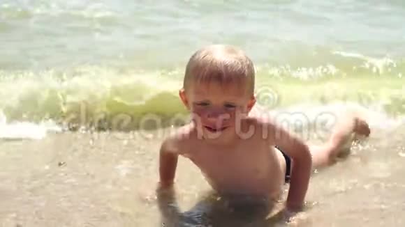 小金发男孩躺在沙滩上的沙滩上慢动作视频的预览图