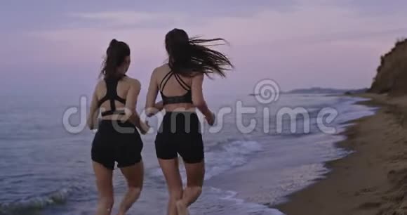 早上两位魅力十足的女士穿着运动服装一起在海滩上奔跑视频的预览图