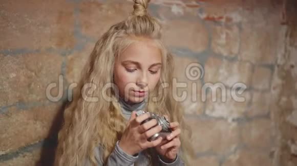 漂亮的女孩在砖墙背景上的老式相机上拍照穿复古相机的女孩视频的预览图